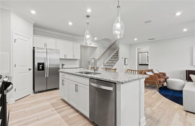 kitchen with stainless steel appliances, open floor plan, a sink, and ornamental molding