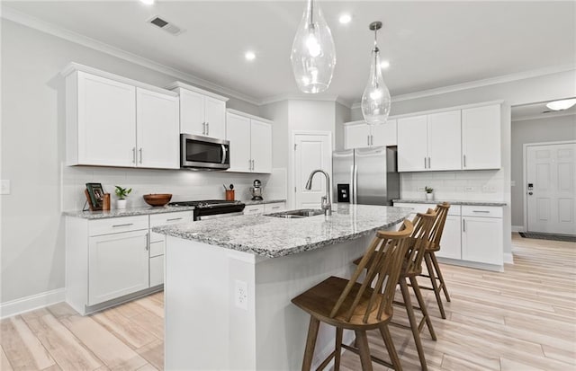 kitchen with appliances with stainless steel finishes, an island with sink, and white cabinetry