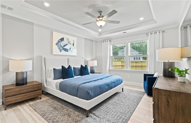 bedroom with ceiling fan, light hardwood / wood-style floors, a tray ceiling, and crown molding