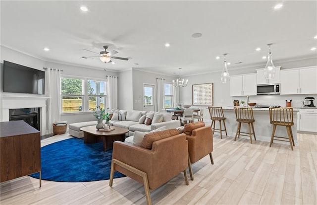 living room featuring a high end fireplace, crown molding, and ceiling fan with notable chandelier