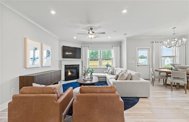 living room with crown molding, a fireplace, ceiling fan with notable chandelier, and light hardwood / wood-style floors