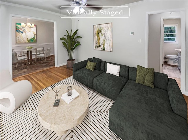 living area featuring ceiling fan with notable chandelier, ornamental molding, wood finished floors, and baseboards