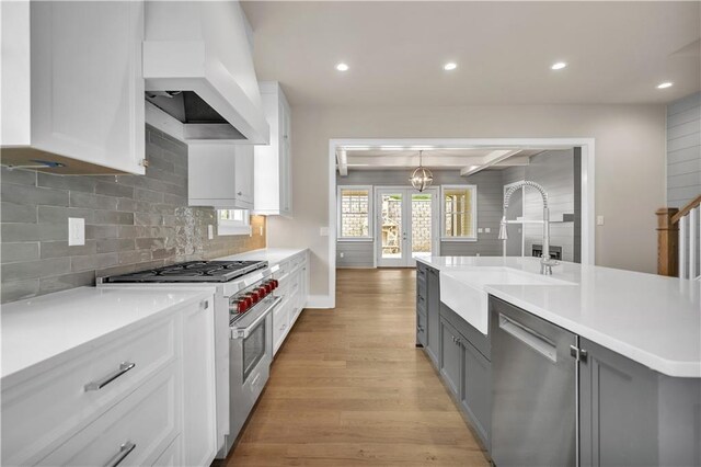 kitchen with sink, white cabinetry, custom exhaust hood, appliances with stainless steel finishes, and light hardwood / wood-style floors