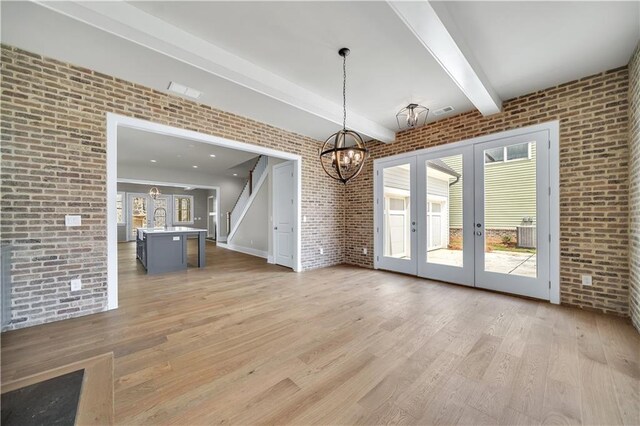 interior space with an inviting chandelier, brick wall, french doors, and light wood-type flooring