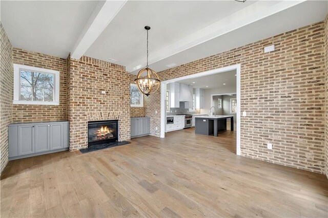 unfurnished living room featuring sink, light wood-type flooring, beam ceiling, brick wall, and a chandelier