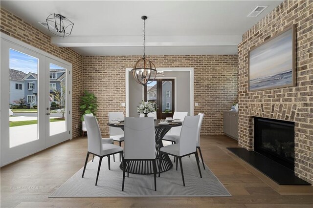 dining room featuring an outdoor brick fireplace, french doors, light hardwood / wood-style floors, brick wall, and a chandelier