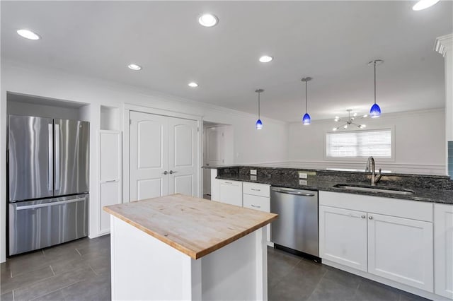 kitchen featuring butcher block countertops, ornamental molding, appliances with stainless steel finishes, white cabinetry, and a sink