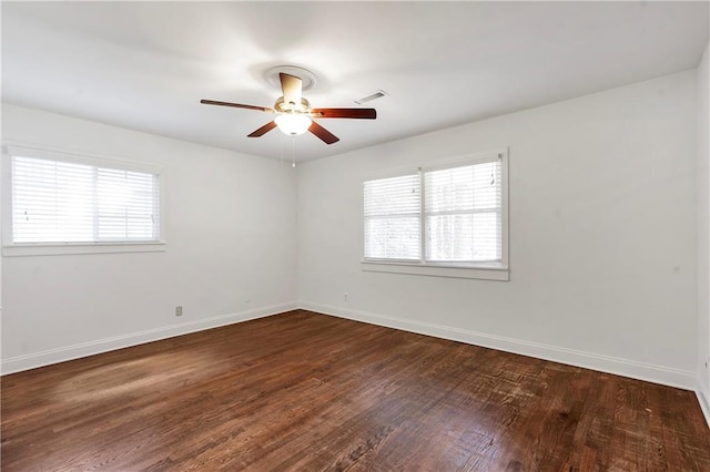 empty room featuring a wealth of natural light, visible vents, baseboards, and dark wood-style floors