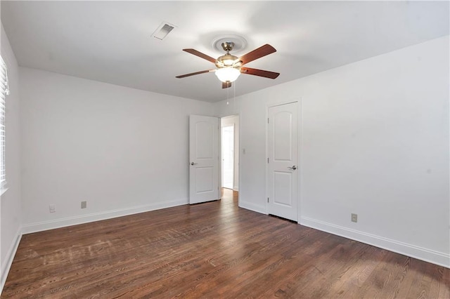 spare room with dark wood finished floors, visible vents, a ceiling fan, and baseboards