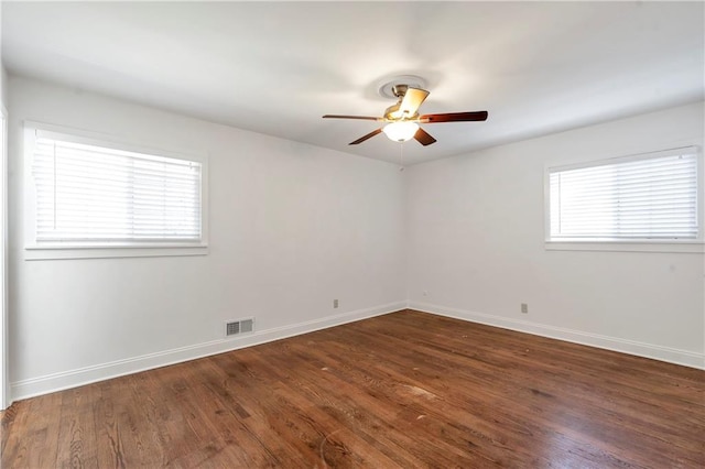 empty room with dark wood finished floors, visible vents, ceiling fan, and baseboards