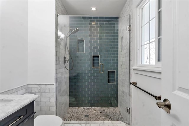 full bath with a shower stall, toilet, vanity, wainscoting, and tile walls