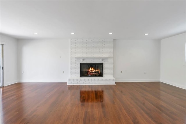 unfurnished living room with recessed lighting, baseboards, a brick fireplace, and wood finished floors