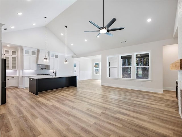 kitchen with white cabinets, light hardwood / wood-style floors, an island with sink, and high vaulted ceiling