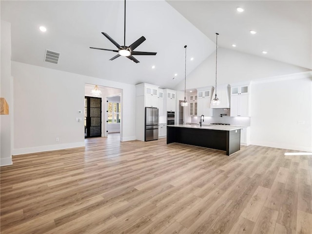 kitchen with high vaulted ceiling, hanging light fixtures, a kitchen island with sink, light hardwood / wood-style flooring, and white cabinets