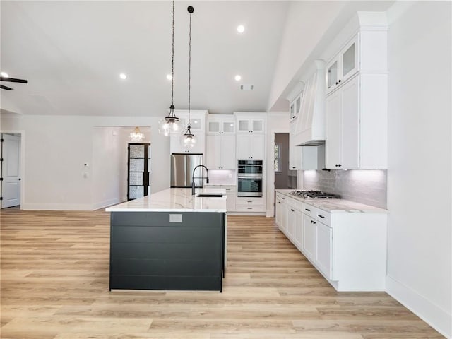 kitchen with a kitchen island with sink, hanging light fixtures, sink, lofted ceiling, and light hardwood / wood-style flooring