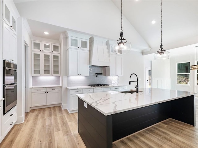 kitchen featuring white cabinetry, sink, custom exhaust hood, a kitchen island with sink, and pendant lighting