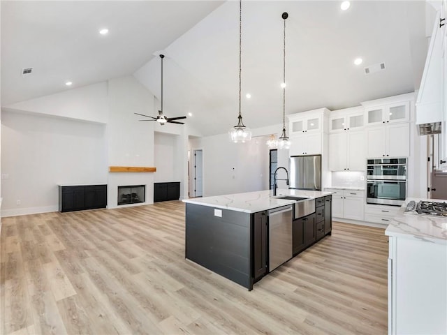 kitchen featuring stainless steel appliances, sink, a large fireplace, white cabinets, and light wood-type flooring