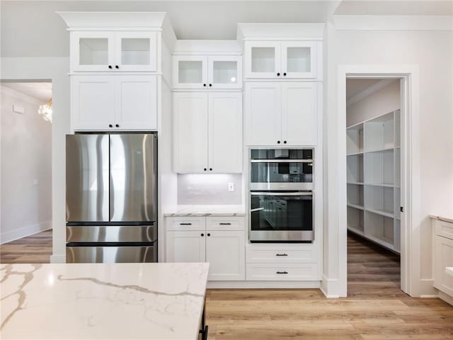 kitchen with stainless steel appliances, white cabinetry, light stone counters, backsplash, and light wood-type flooring