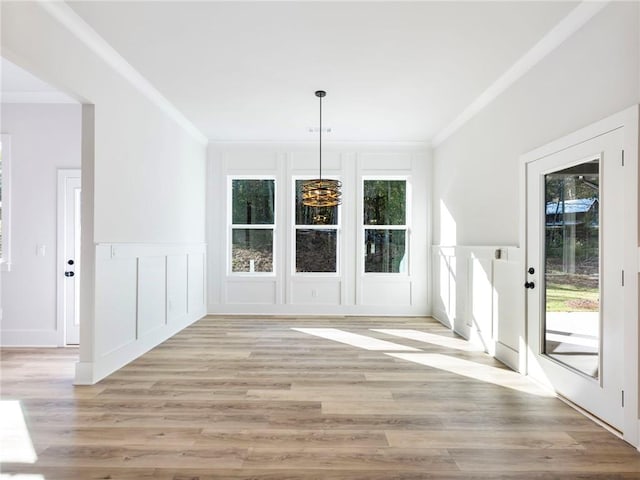 unfurnished dining area featuring light wood-type flooring, an inviting chandelier, ornamental molding, and plenty of natural light