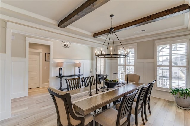 dining room featuring a decorative wall, wainscoting, light wood finished floors, beamed ceiling, and an inviting chandelier