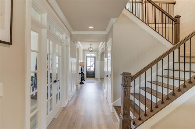 entryway with a decorative wall, a wainscoted wall, french doors, light wood finished floors, and crown molding