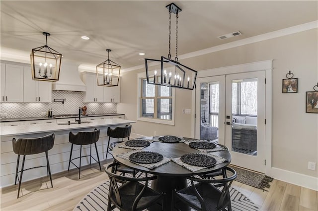 dining room featuring visible vents, baseboards, french doors, ornamental molding, and light wood finished floors