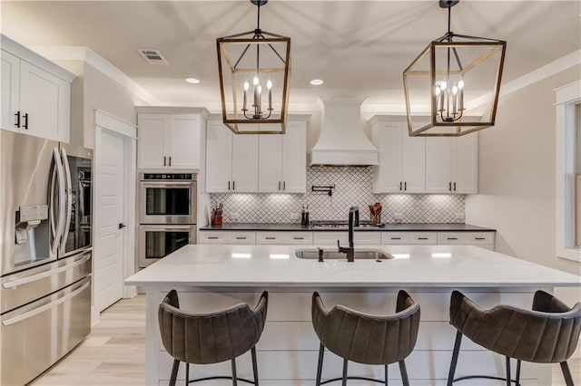 kitchen with a sink, white cabinets, custom range hood, appliances with stainless steel finishes, and crown molding