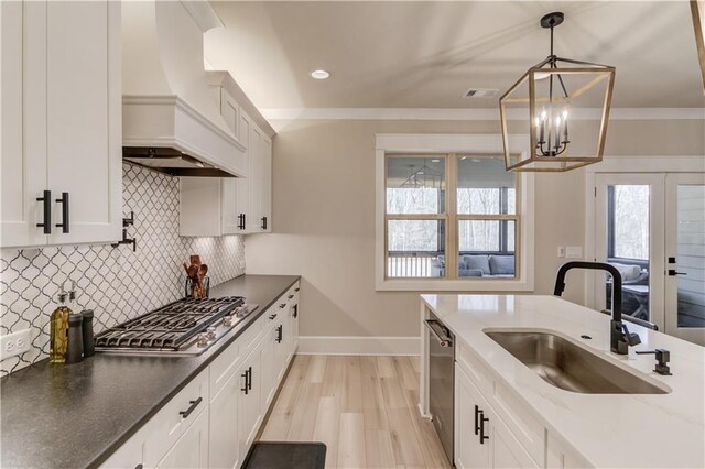 kitchen with stainless steel appliances, a sink, white cabinetry, custom exhaust hood, and decorative light fixtures