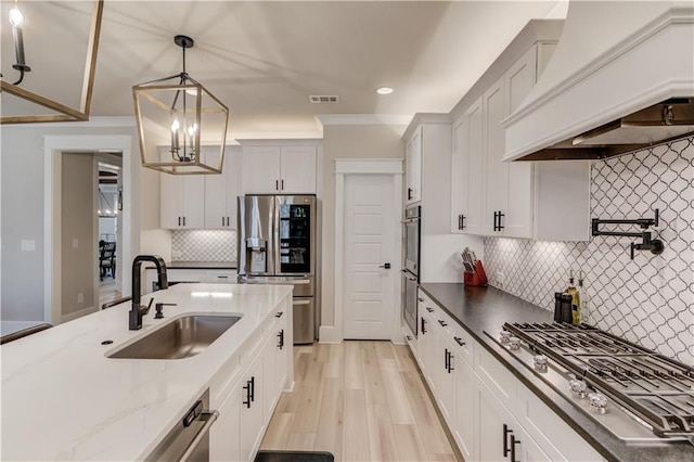 kitchen with stainless steel appliances, a sink, white cabinetry, custom exhaust hood, and pendant lighting