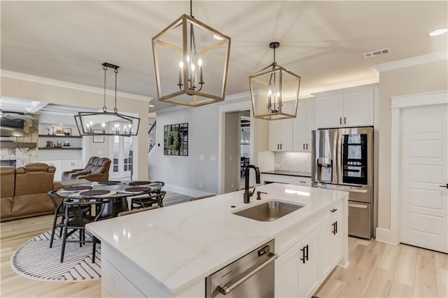 kitchen with pendant lighting, stainless steel appliances, open floor plan, a sink, and an island with sink