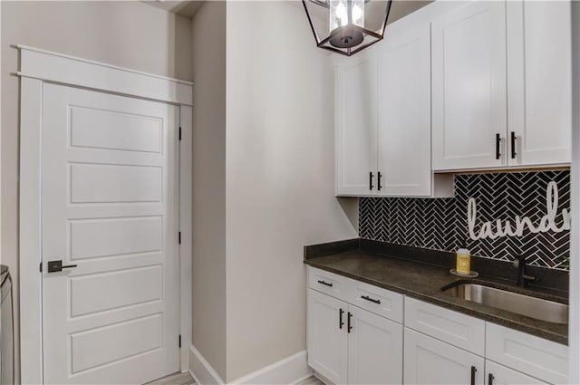 interior space with decorative backsplash, white cabinets, a sink, and dark stone countertops