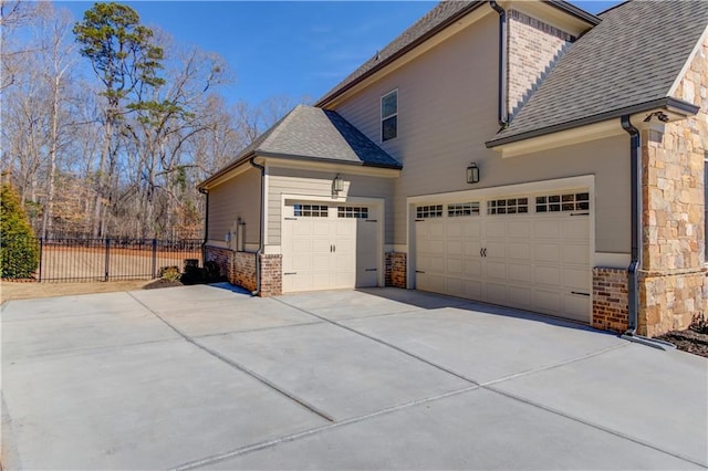 view of home's exterior with a garage, brick siding, a shingled roof, fence, and driveway