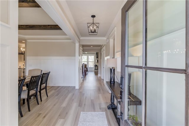 foyer with wainscoting, crown molding, light wood-type flooring, a decorative wall, and a notable chandelier