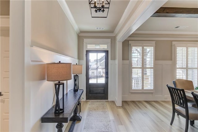 foyer entrance featuring light wood-style floors, plenty of natural light, ornamental molding, and a wainscoted wall