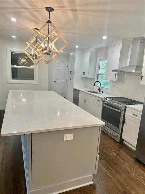 kitchen with gas stove, wall chimney range hood, white cabinets, pendant lighting, and sink