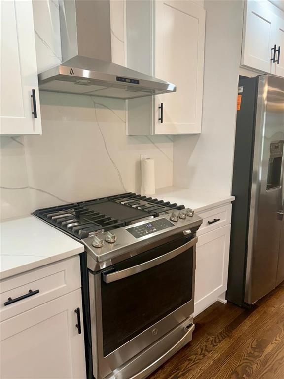 kitchen featuring wall chimney exhaust hood, appliances with stainless steel finishes, dark hardwood / wood-style flooring, and white cabinets