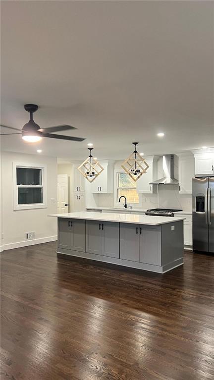 kitchen featuring a center island with sink, stainless steel fridge, wall chimney exhaust hood, pendant lighting, and dark hardwood / wood-style floors