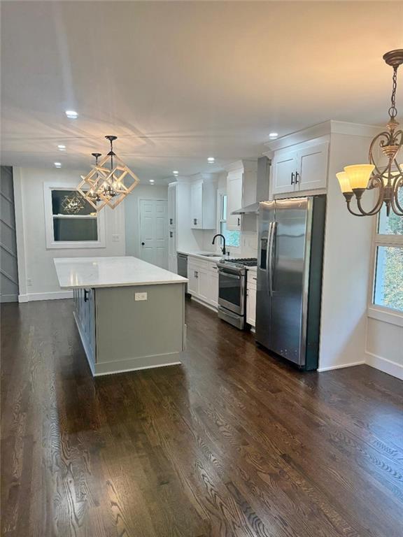 kitchen featuring dark hardwood / wood-style flooring, stainless steel appliances, wall chimney exhaust hood, pendant lighting, and white cabinets