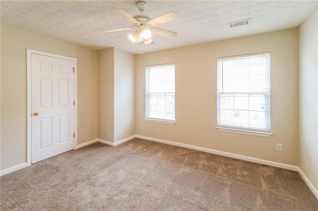 carpeted empty room with ceiling fan, baseboards, visible vents, and a textured ceiling