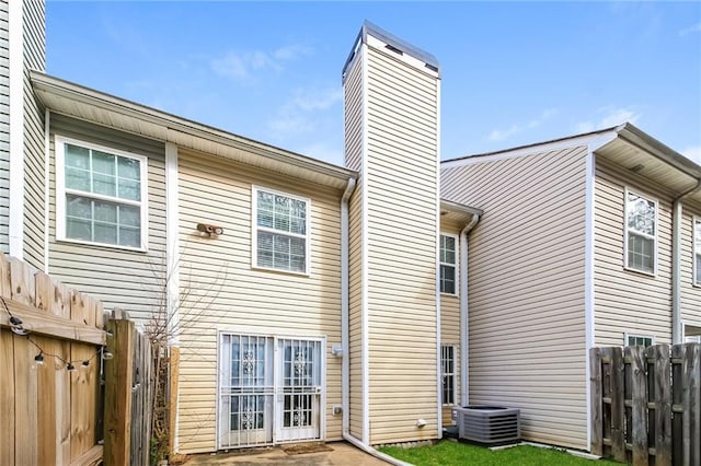 back of property featuring fence, central AC, and a chimney