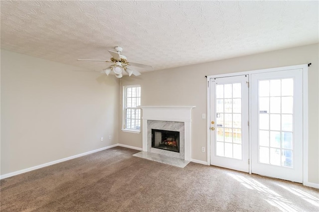 unfurnished living room featuring carpet flooring, baseboards, ceiling fan, and a high end fireplace