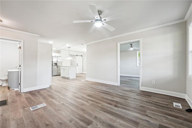 unfurnished living room featuring a barn door, ornamental molding, and hardwood / wood-style floors