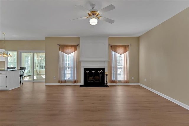 unfurnished living room featuring ceiling fan with notable chandelier, wood finished floors, a fireplace with flush hearth, and baseboards