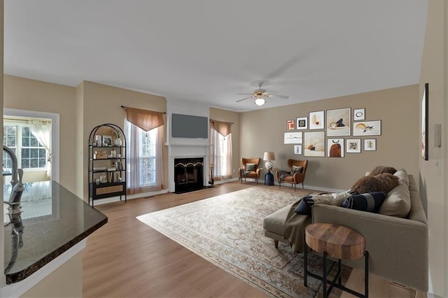 living room with light wood-style floors, plenty of natural light, a ceiling fan, and a fireplace with flush hearth