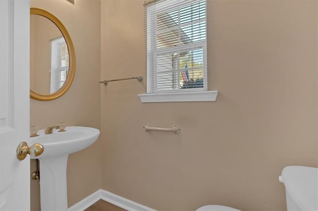 half bath with baseboards, a sink, and toilet