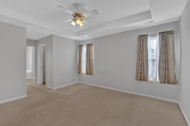 unfurnished room featuring visible vents, baseboards, light colored carpet, ceiling fan, and a tray ceiling