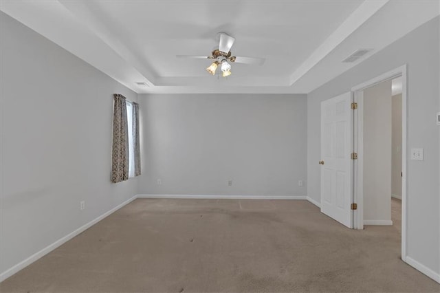 carpeted spare room featuring ceiling fan, a tray ceiling, visible vents, and baseboards