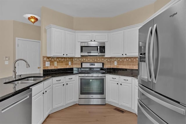 kitchen featuring visible vents, white cabinets, stainless steel appliances, light wood-style floors, and a sink