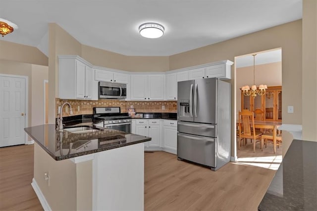 kitchen with appliances with stainless steel finishes, a peninsula, an inviting chandelier, light wood-style floors, and a sink