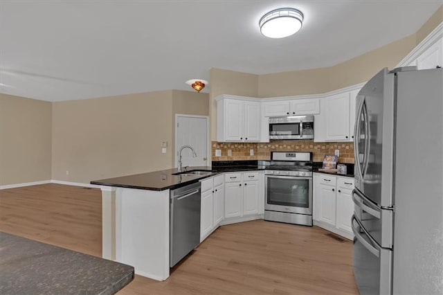 kitchen featuring stainless steel appliances, a peninsula, a sink, light wood finished floors, and tasteful backsplash